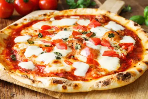Pyszne ciasto na pizzę bez wyrastania, z pomidorami, mozzarellą i bazylią, na drewnianej desce.