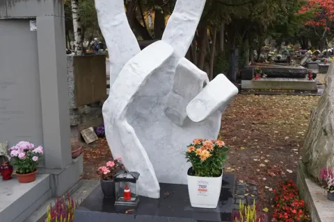 Monumentalna dłoń z symbolem pokoju na tle cmentarza. Wiele nagrobków tworzy ten zadumany zespół.