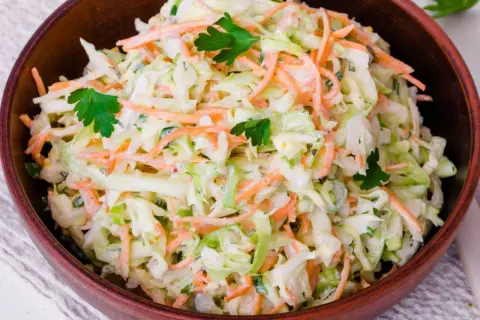 Klasyczny coleslaw w drewnianej misce, pełen chrupiącej kapusty i marchewki, udekorowany natką pietruszki.