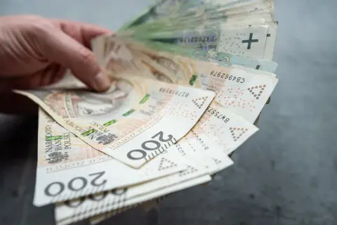 Dłoń trzyma plik banknotów 200 zł. Czy współwłaściciel konta może wypłacić pieniądze po śmierci właściciela?