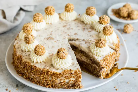 Eine köstliche Giotto Torte, verziert mit Sahnetuffs und Haselnusskugeln, umgeben von gehackten Nüssen.