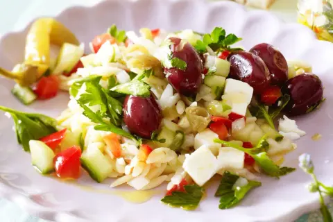 Ein erfrischender griechischer Orzo Salat mit Oliven, Feta, Gurken und Tomaten, garniert mit frischer Petersilie.
