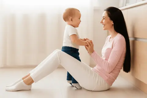 Une mère et son bébé se tiennent la main, souriants, assis sur le sol.