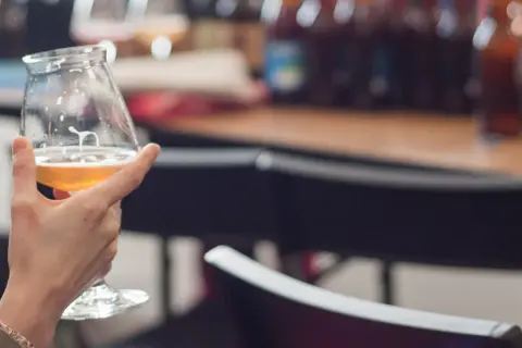 Degustacja piwa na festiwalu. Złocisty trunek w kieliszku, w tle butelki i atmosfera dobrej zabawy.