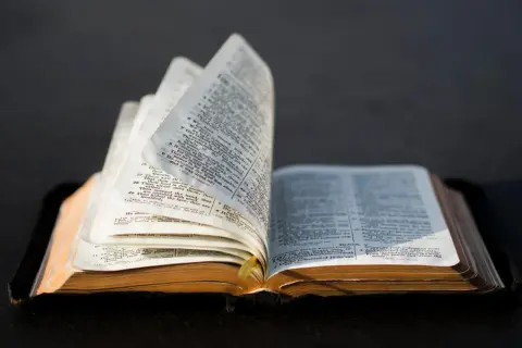 Otwarta Biblia, której strony wirują, ukazując tekst. Syn sema, jakby szukający odpowiedzi w słowach.