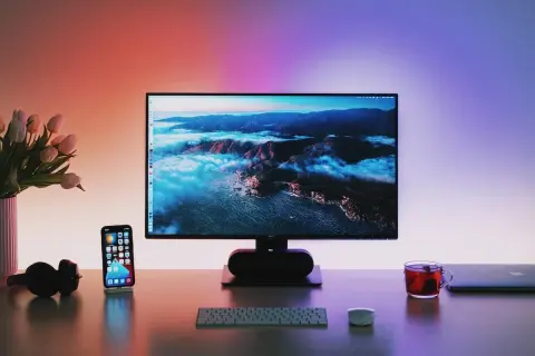 Biurko z monitorem wyświetlającym krajobraz, telefonem, słuchawkami i kubkiem herbaty.