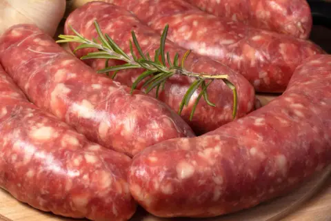 Świeża salsiccia z gałązką rozmarynu i czosnkiem w tle, gotowa do grillowania.