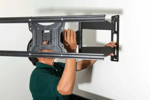 Man in green shirt mounting a TV bracket to the wall.