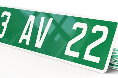 Plaque verte voiture avec "123 AV 22" en blanc. D'autres plaques similaires sont empilées en dessous.