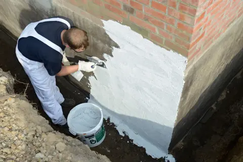 Mann dichtet mit Spachtel die Außenwand ab. Ein Eimer mit Abdichtmasse steht bereit.
