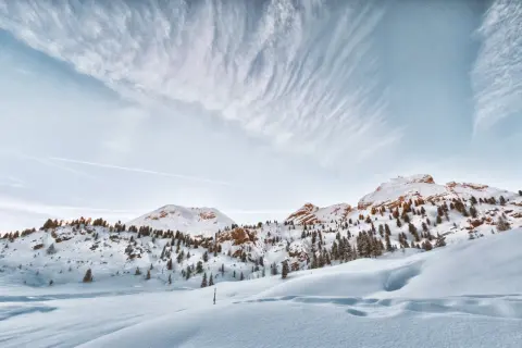Paysage de montagne enneigé, avec des sapins clairsemés sur les pentes. Le ciel est bleu pâle avec des nuages filandreux. Une belle neige photo.