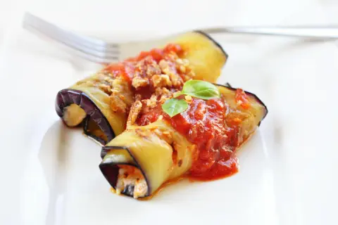 Deliziosi involtini di melanzane alla siciliana, ripieni e conditi con sugo rosso e basilico fresco, pronti per essere gustati.