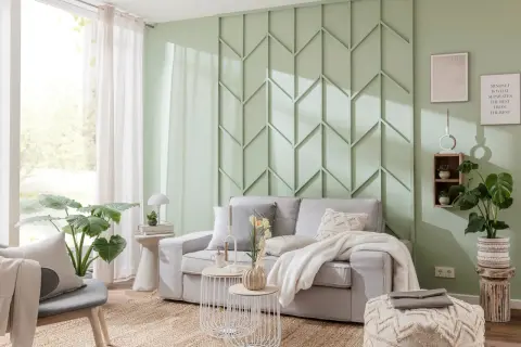 Eine stilvolle Wand hinter der Couch gestalten mit einem geometrischen Paneel in Mintgrün. Gemütliche Atmosphäre mit hellgrauem Sofa, Kissen und Decke.