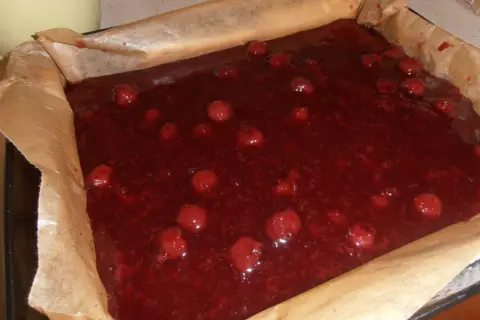 Gotowe do pieczenia ciasto bajka z wiśniami w blaszce wyłożonej papierem. Słodka, czerwona masa z całymi owocami.