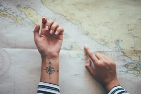 Hände über einer Seekarte, eine mit einem Kompass-Tattoo, das an ein Partner Tattoo Koordinaten erinnert.