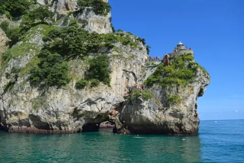 Escaleras y faros en Cantabria, con gente disfrutando del mar y la costa rocosa.
