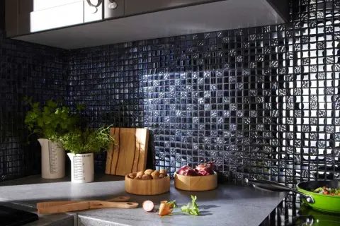 Crédence noire brillante, idéale pour une cuisine moderne. Des herbes fraîches, des oignons et des noix sur le plan de travail. Quelle crédence choisir pour un style audacieux ?