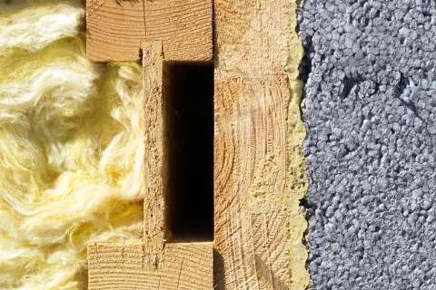 Przekrój ściany: z jednej strony puszysta wełna mineralna, z drugiej szary styropian, pośrodku drewniana konstrukcja.