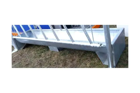 Metalowy żłób na paszę, stojący na trawie, gotowy do karmienia zwierząt.