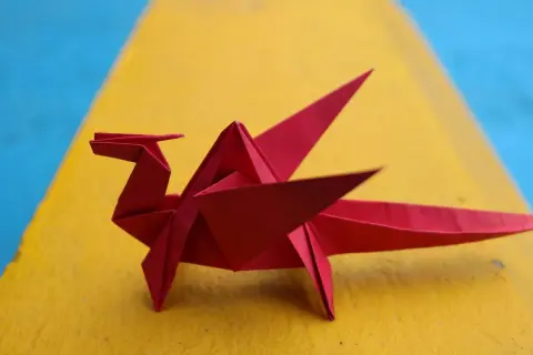 Un dragón rojo de papiroflexia fácil descansa sobre una superficie amarilla y azul.