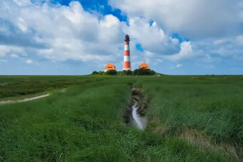 Leuchtturm Westerheversand, ein ikonischer fotospot in Schleswig-Holstein, ragt über grünes Marschland unter dramatischem Himmel.