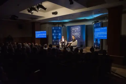 Conference photography captures a panel discussion on a stage with two speakers, audience members in the foreground, and Bloomberg branding.