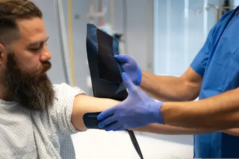 Medyk w niebieskich rękawiczkach zakłada mankiet na ramię pacjenta. Badanie może pomóc ocenić poziom lipoproteiny, co to jest i jak wpływa na zdrowie.