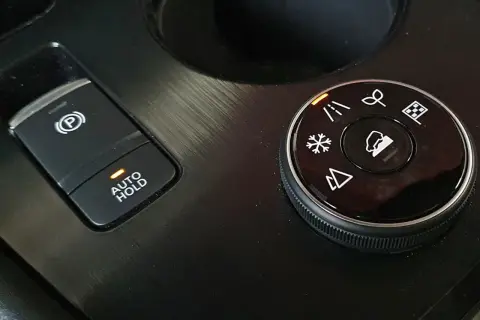 Przycisk "AUTO HOLD" z pomarańczową diodą obok hamulca ręcznego. Obok pokrętło wyboru trybów jazdy: terenowe, śnieg, normalne.