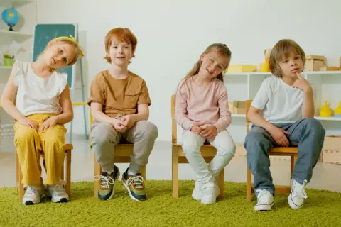 Cztery dzieci siedzą na krzesłach. Jedno z nich, z rudymi włosami, uśmiecha się, być może zmagając się z zaburzeniami neurorozwojowymi.