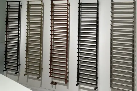 Cinq sèche-serviettes de différentes couleurs (noir, bronze, marron, noir, gris) sont alignés. La hauteur de ces sèche-serviettes est impressionnante.