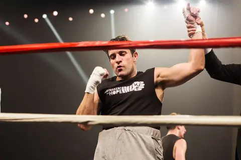 A boxer's arm is raised in victory, a moment of triumph in amateur vs professional boxing. The crowd roars as the referee declares the winner.