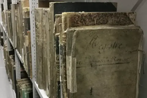 Des registres anciens, certains marqués "archive 07", s'alignent sur des étagères métalliques, témoins silencieux du temps.