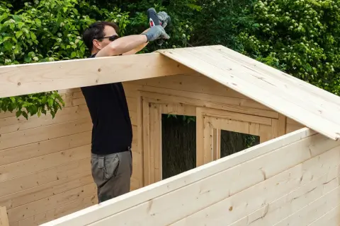 Hombre construyendo una caseta de madera. ¿Cuál es la mejor madera? Esta parece ser de pino, ligera y fácil de trabajar.