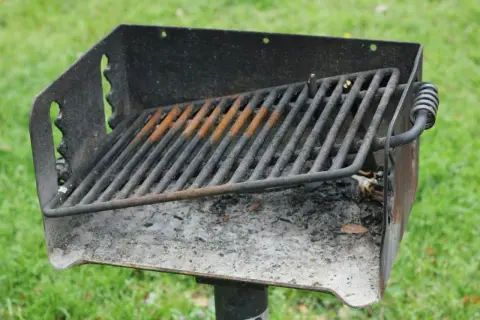 Ett rostigt grillgaller med aska under, redo för nästa grillkväll i parken.