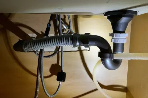 Pod zlewem widać instalację hydrauliczną z syfonem i elastycznym wężem odpływowym. Widać też trójnik, który rozdziela odpływ.