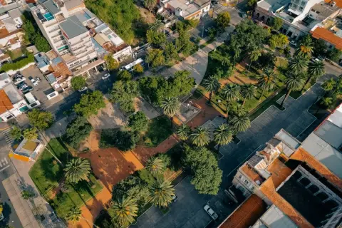 Un parco urbano rigenerato, con palme e alberi, circondato da edifici residenziali e commerciali.