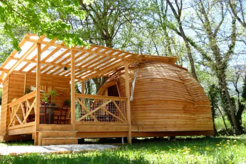 Cabane en bois et dôme de glamping Paca, avec terrasse et table extérieure, dans un cadre verdoyant.