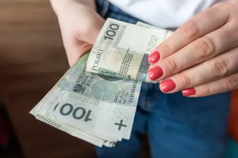 Dłonie z czerwonymi paznokciami trzymają stos banknotów 100 zł. To polska stopa referencyjna NBP.