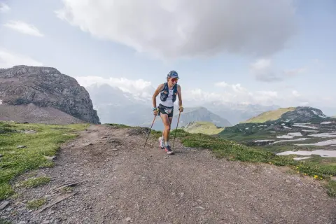 Corredor/a de montaña en un sendero rocoso, con bastones y vistas alpinas. Esto es trail running, pura aventura.