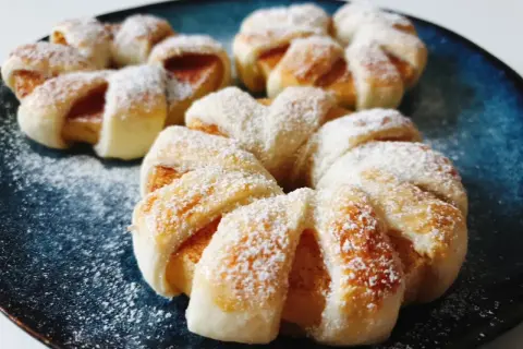 Pyszne ciasto francuskie z jabłkami, posypane cukrem pudrem, prezentuje się apetycznie na granatowym talerzu.