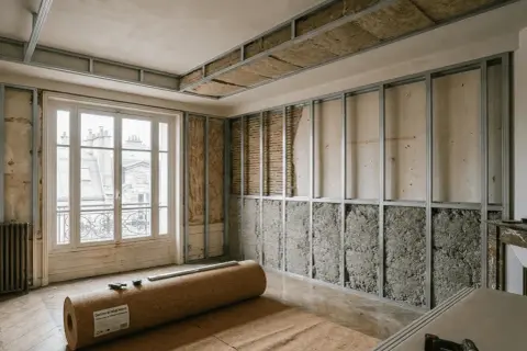 Travaux en cours pour isoler phoniquement cette pièce. Des ossatures métalliques sont installées sur les murs et le plafond, prêtes à accueillir l'isolant. Un rouleau de liège est au sol.