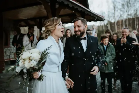 Szczęśliwa para młoda, w otoczeniu gości, świętuje swoje wesele w adwencie. Sypią się płatki, tworząc magiczną atmosferę.