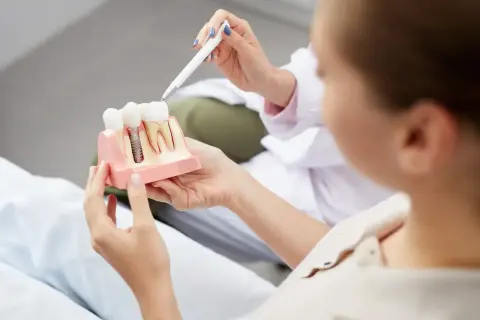 Dentysta wyjaśnia pacjentce budowę implantu zębowego, odpowiadając na pytanie: czy implanty są bezpieczne.