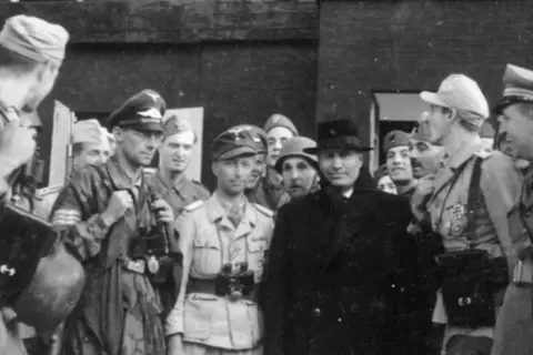 Grupp av män, varav en med hatt och rock, möjligen Otto Skorzeny, omgiven av militärer i uniform.