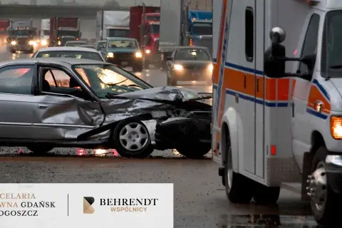 Wypadek w drodze do pracy. Zmiażdżony srebrny samochód i karetka na mokrej drodze.