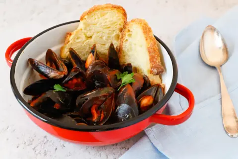 Un invitante guazzetto di cozze in una pentola rossa, accompagnato da pane croccante e una forchetta.