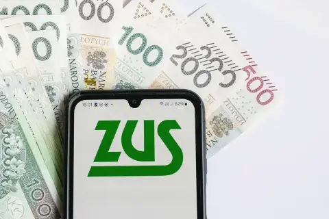 Telefon z logo ZUS na tle polskich banknotów. Może to symbolizować zwrot składki zdrowotnej lub inne rozliczenia z ZUS.