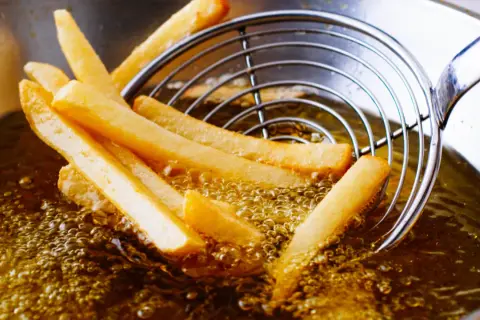 Patatine fritte dorate che sfrigolano nell'olio di oliva, pronte per essere gustate.
