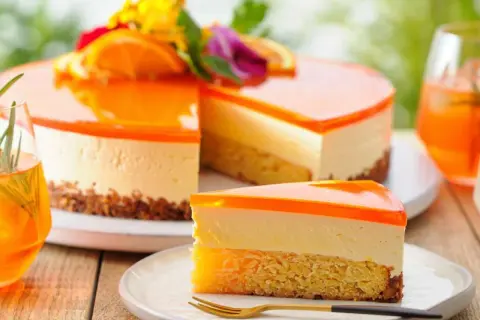 Erfrischende Aperol Torte mit Orangen-Gelee-Schicht und cremigem Käsekuchen. Ein Stück auf einem Teller mit Gabel.