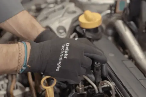 Manos con guantes negros trabajando en un motor diésel, manipulando un inyector.